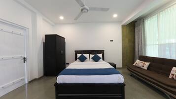 A bedroom with a bed, a ceiling fan, a wardrobe, a sofa, and a window with curtains.