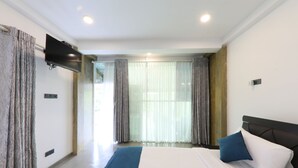 Een moderne hotelkamer met een groot bed, een flatscreen televisie aan de muur en uitzicht op het omliggende landschap door grote ramen.
