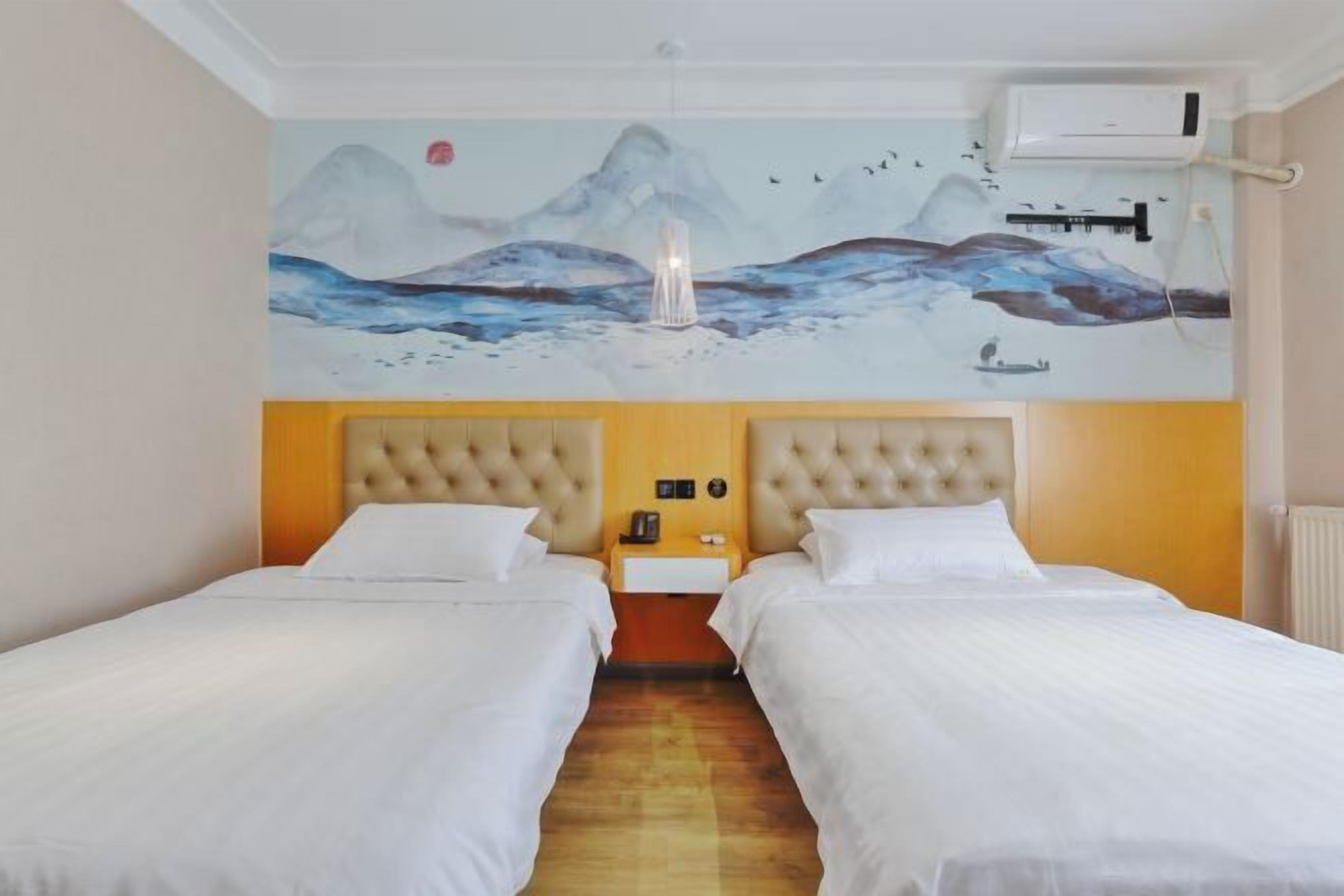 A hotel room with two beds, a mural of mountains and birds, a bedside lamp, and an air conditioning unit.