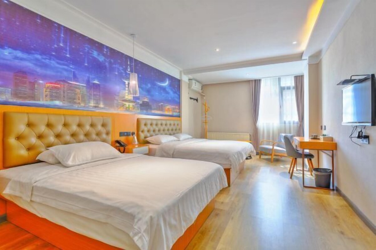 A hotel room with two beds, a desk, a chair, a TV, and a cityscape mural on the wall.