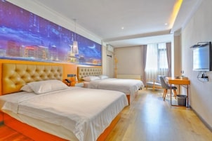 Habitación de hotel con dos camas, un escritorio, una silla, un televisor y un mural con vista a la ciudad.