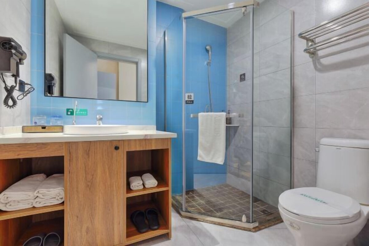 A bathroom with a shower, toilet, and wooden shelves with towels and slippers.