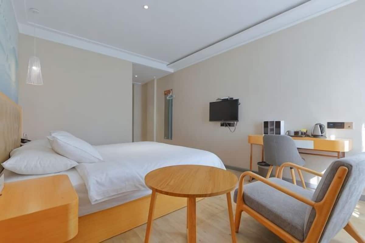 A hotel room with a bed, a desk, a chair, a TV, and a small table.