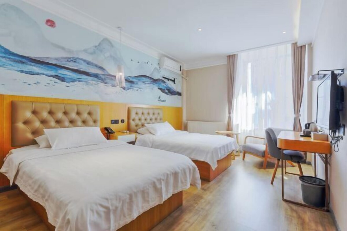 A hotel room with two beds, a desk, a chair, and a large mural on the wall.