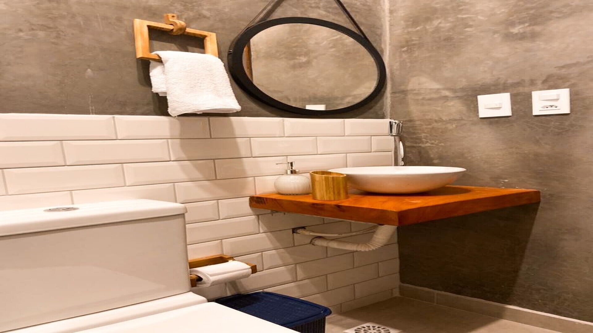 Un baño con inodoro, lavamanos sobre estante de madera, toallero y espejo.