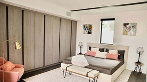 Een slaapkamer met een bed, een bankje, een stoel, twee nachtkastjes en kunstwerken aan de muren.