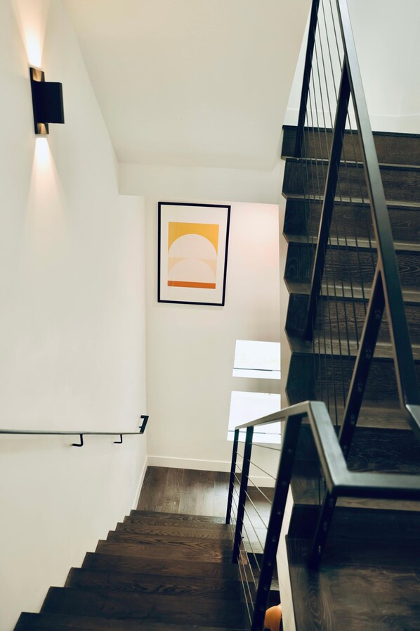 A staircase with dark wooden steps and black railings, leading to a landing with a framed artwork and a wall-mounted light fixture.