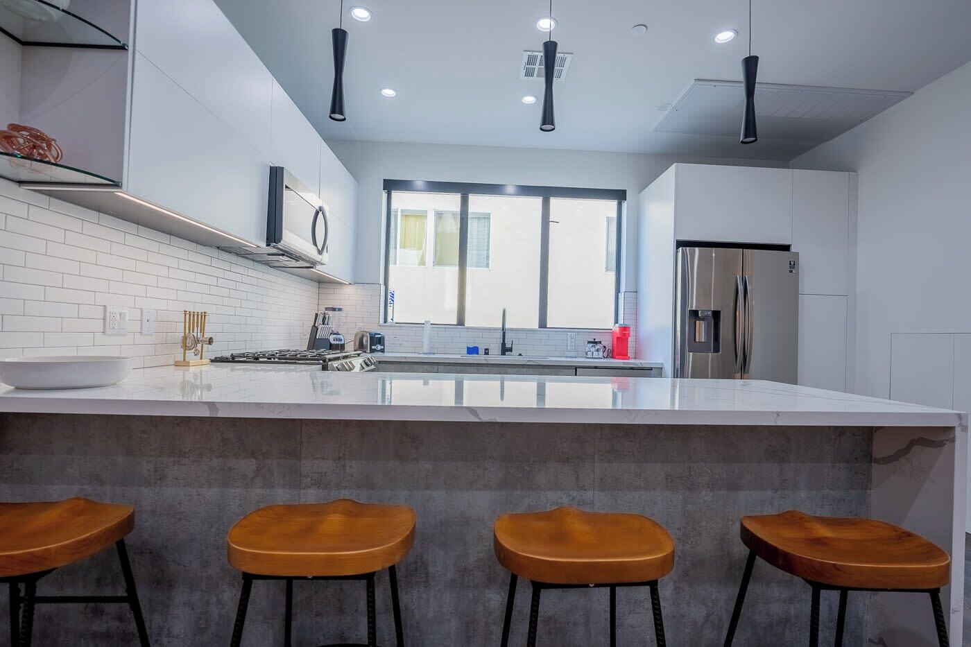 Une cuisine moderne dotée d’un grand îlot central, de tabourets de bar, d’appareils électroménagers en acier inoxydable et d’une fenêtre laissant entrer la lumière naturelle.