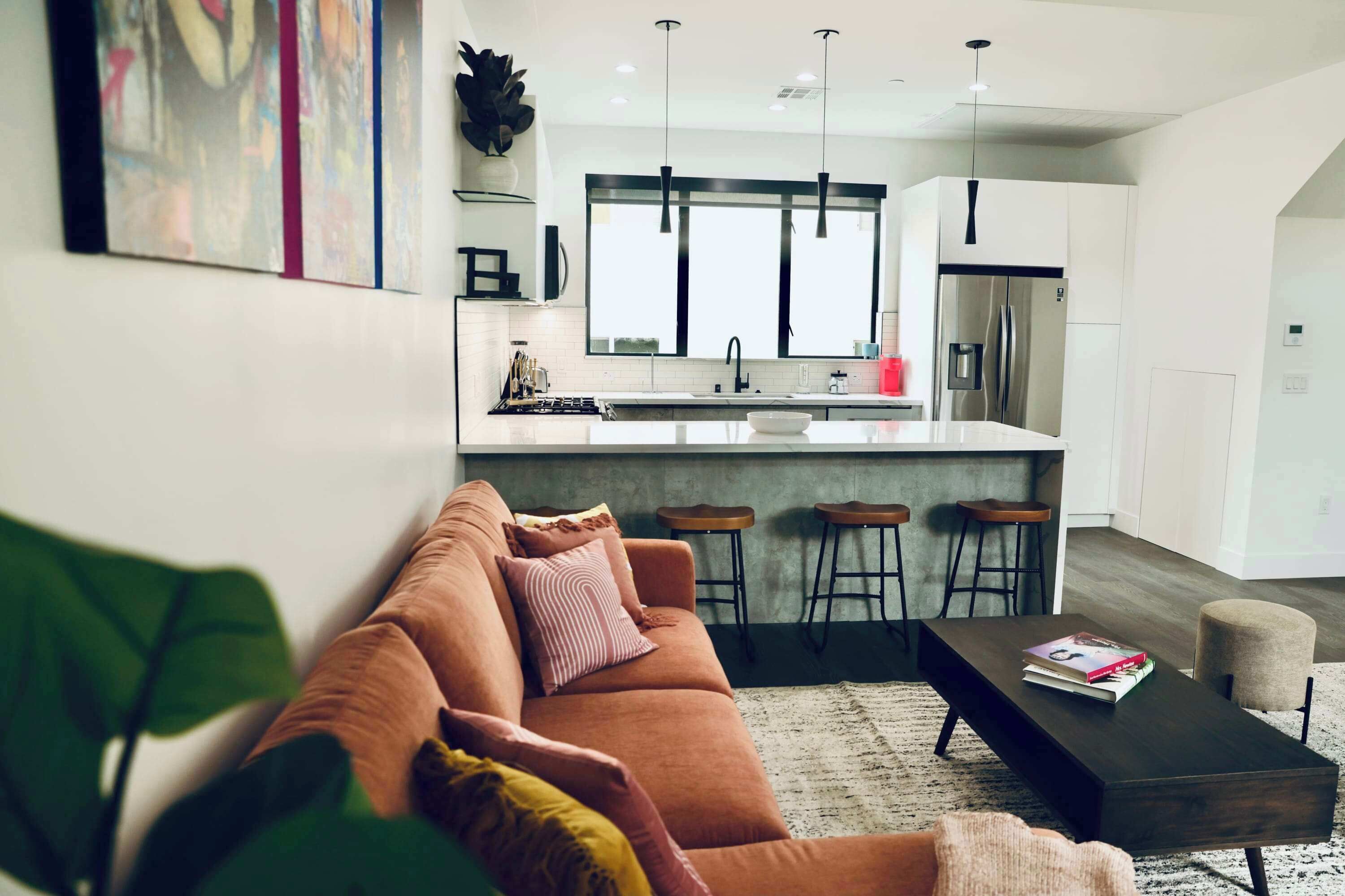 Una cocina moderna con una isla central, taburetes de bar y un sofá en la sala de estar.