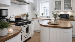 A modern kitchen with white cabinetry, a central island, a stove, and a microwave. - Spacious 12-Bedroom Coastal Retreat Private Annex (Mundesley)