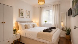 A bedroom with a bed, bedside tables, a wardrobe, a window with curtains, a hanging light fixture, and framed botanical prints on the wall. - Spacious 12-Bedroom Coastal Retreat Private Annex (Mundesley)