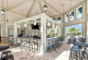 A covered outdoor bar area with seating and a television screen.