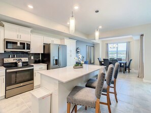 A modern kitchen with stainless steel appliances, a central island with bar stools, and a dining area with a view.