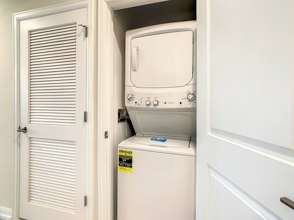 A compact, white laundry room with a built-in washer and dryer, a door with a louvered design, and a visible energy efficiency label.
