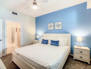 A bedroom with a bed, bedside tables, a ceiling fan, and artwork on the wall.