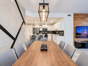 A modern kitchen with white cabinets, a central island, and a dining area with a wooden table and grey chairs.