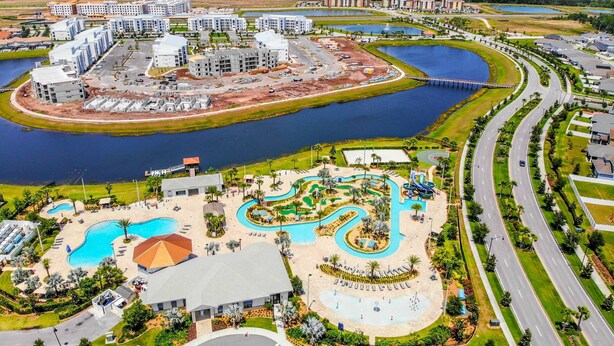 An aerial view of a resort with multiple buildings, a large central pool, and a winding water slide.