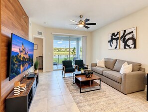 Bright living room with large TV, plush seating, and patio views