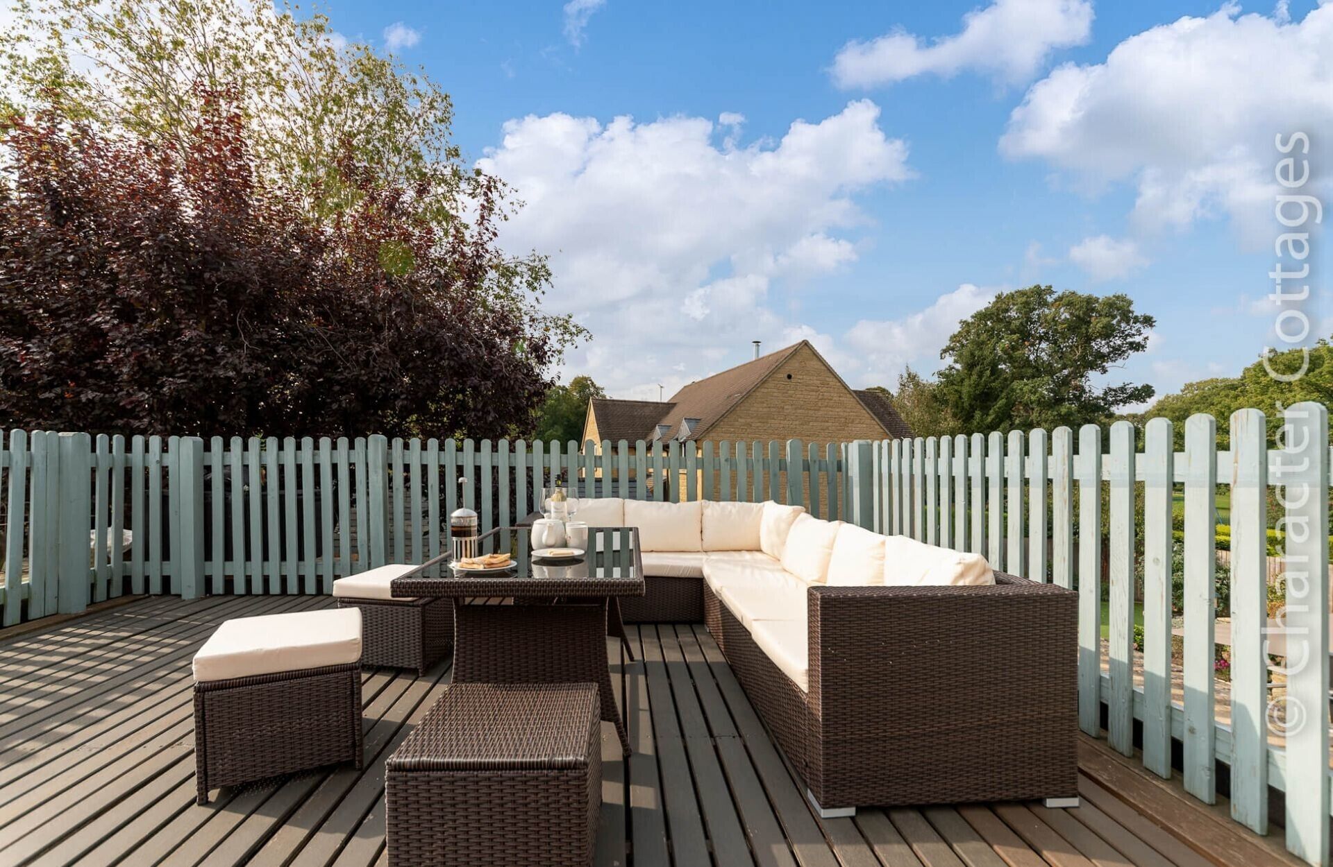 A deck with wicker furniture, including a sofa and ottomans, and a table with a glass set.