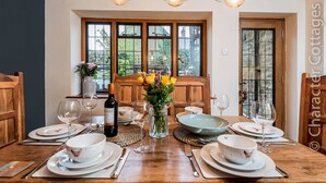 A dining table set for four with white plates, bowls, and cutlery, a bottle of wine, and a vase with flowers. - Eastnor (Moreton-in-Marsh)