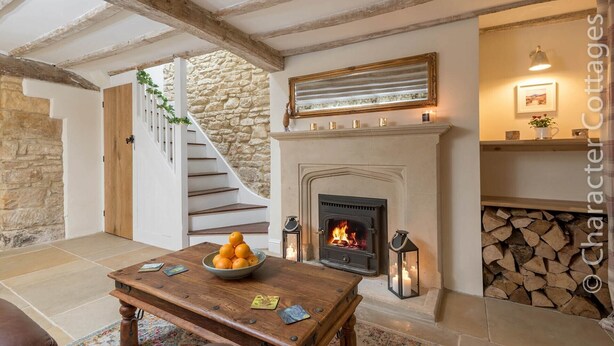 A cozy living room with a fireplace, a stone wall, and a staircase leading upstairs. - Eastnor (Moreton-in-Marsh)