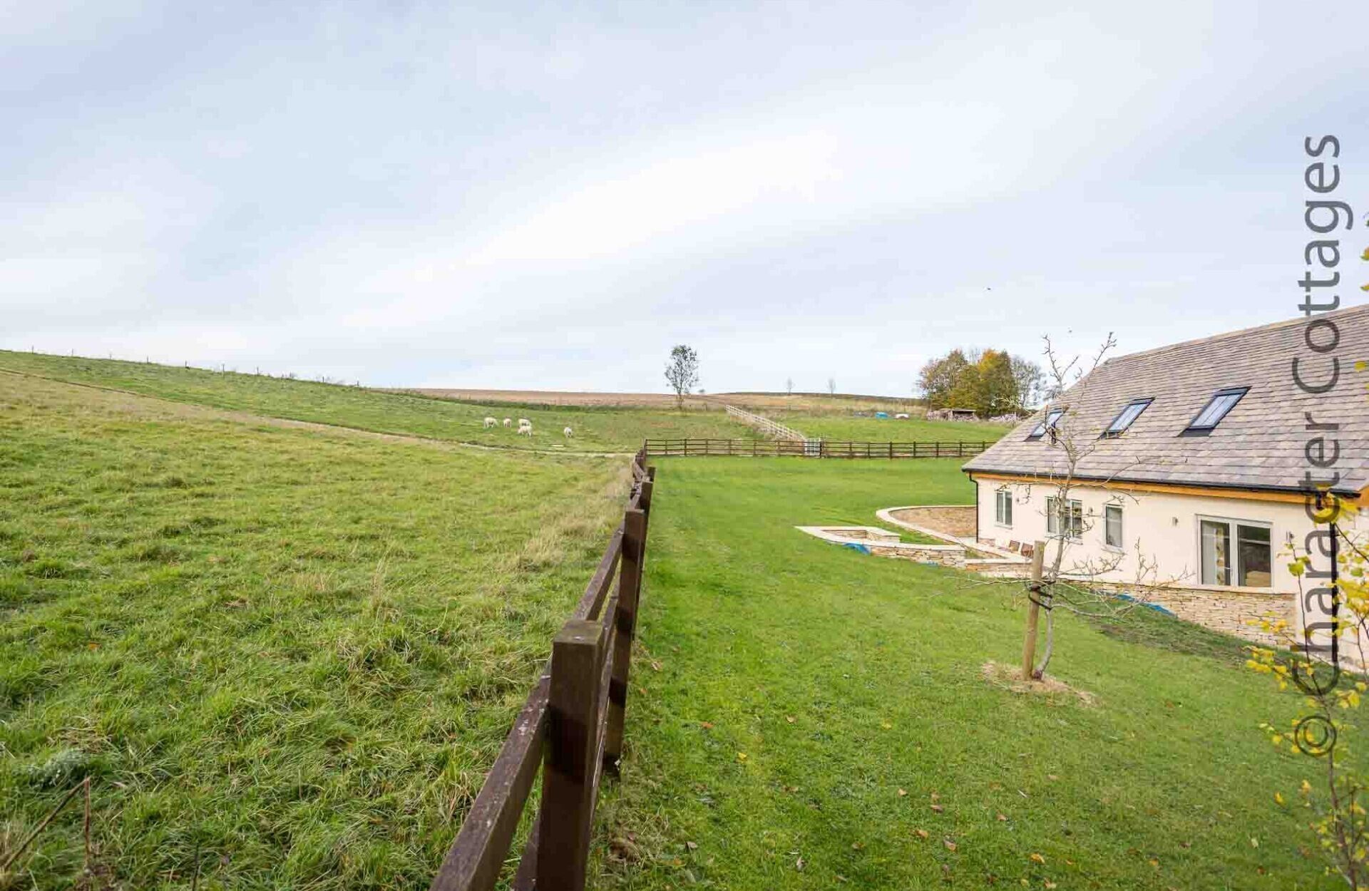 Ein ländliches Anwesen mit eingezäuntem Garten, einem Haus mit Satteldach und freiem Blick auf die umliegende Landschaft.