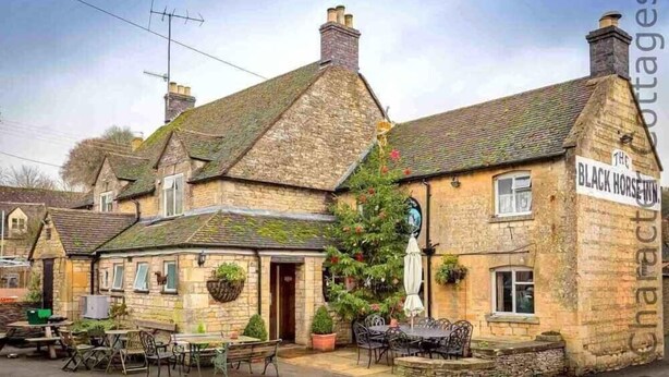A traditional stone building with a sign reading "The Black Horse Inn". - Hetty's Stables (Cheltenham)