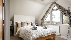 A bedroom with a wooden bed, a window with curtains, a radiator, and a nightstand with a lamp. - Hetty's Stables (Cheltenham)