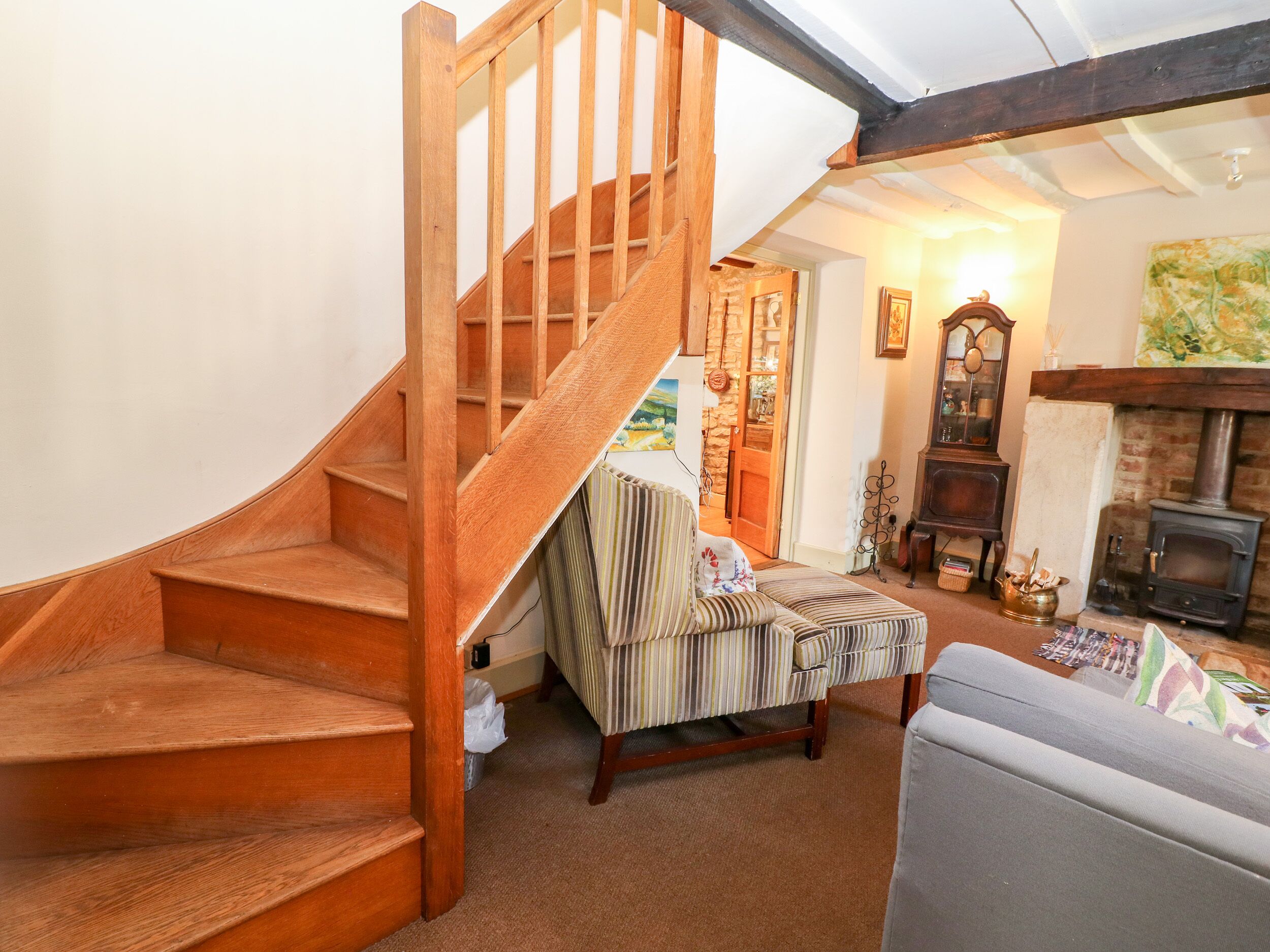 A wooden staircase leading to a loft bedroom with a cozy living area, a fireplace, and a striped armchair.
