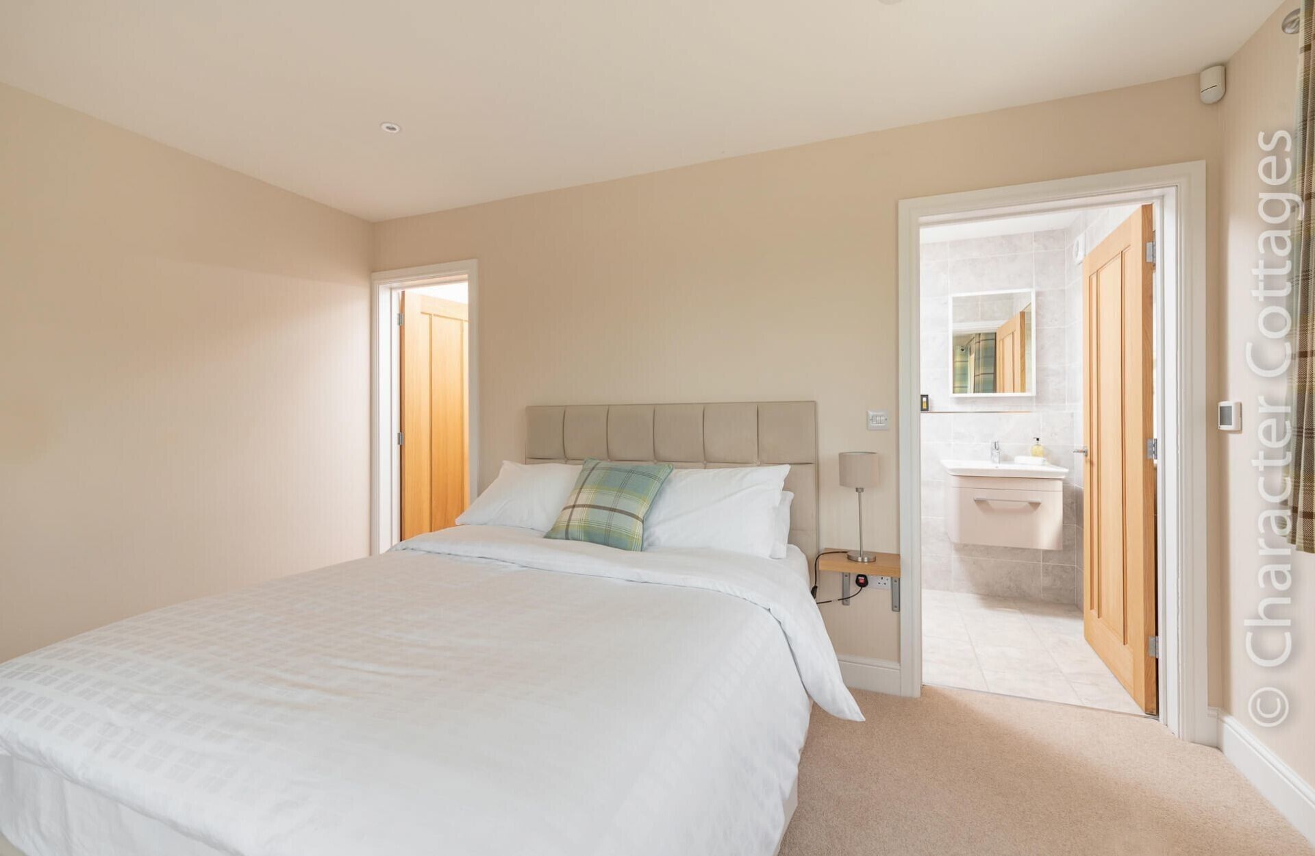 A bedroom with a bed, a nightstand, a bedside table, a mirror, and a bathroom visible through an open door.