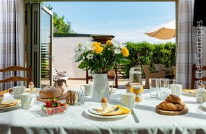 An outdoor dining area with a table set for breakfast, including bread, strawberries, and a croissant.