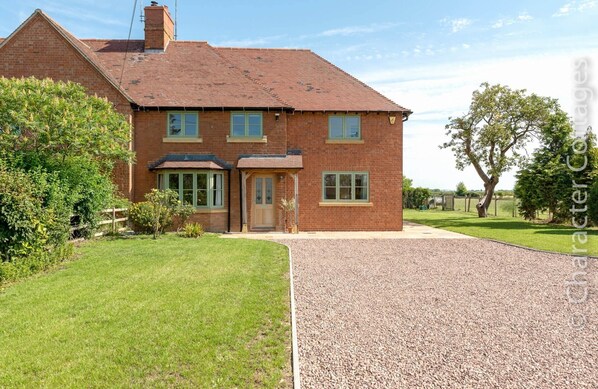 A two-story brick house with a tiled roof, a front porch, and a gravel driveway.