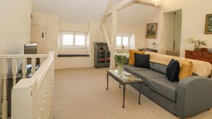 A spacious living area with a grey sofa, a coffee table, and a bookshelf. - The Apartment (Cheltenham)