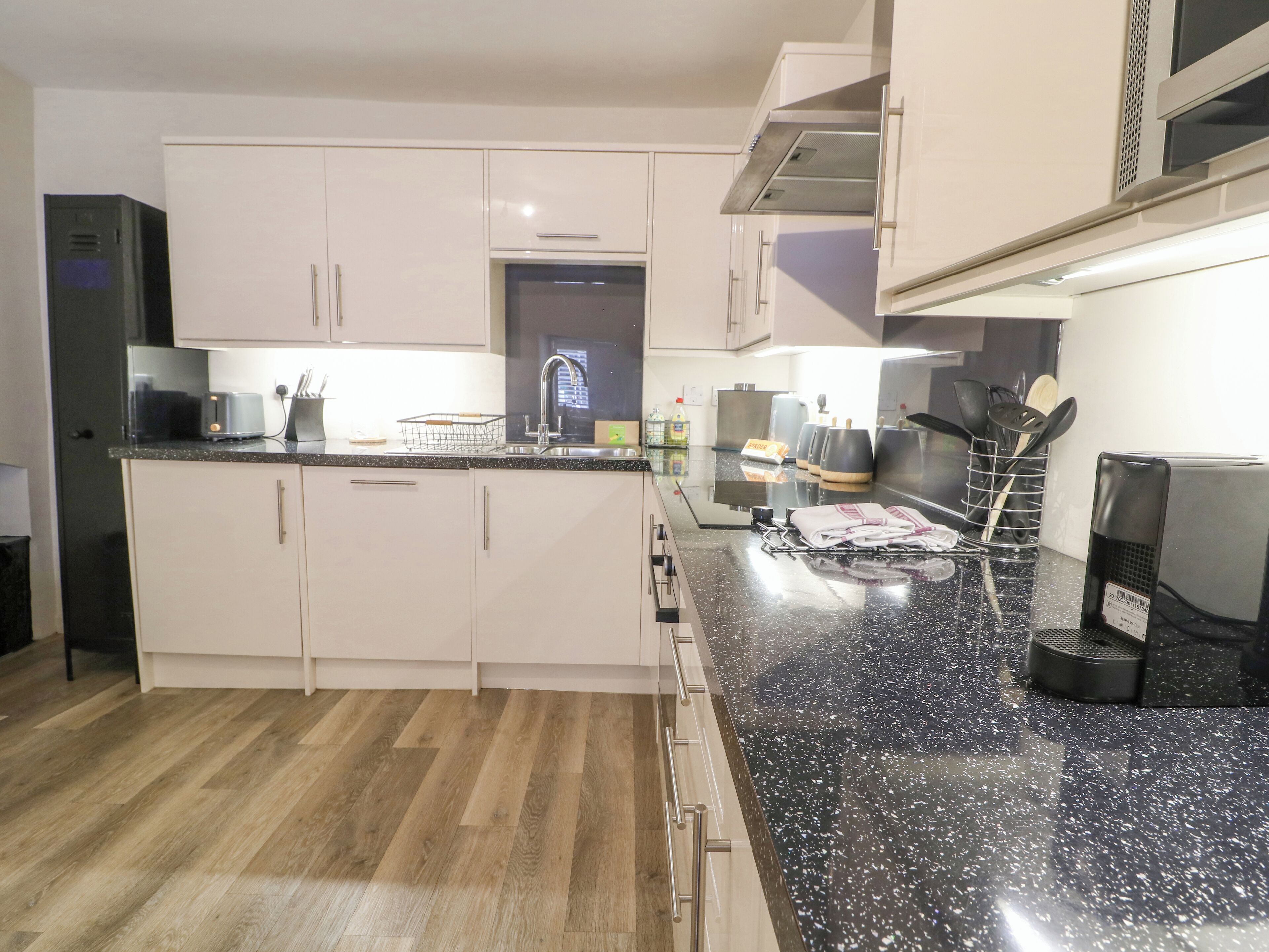 Una cocina moderna con armarios blancos, encimera negra y suelo de madera.