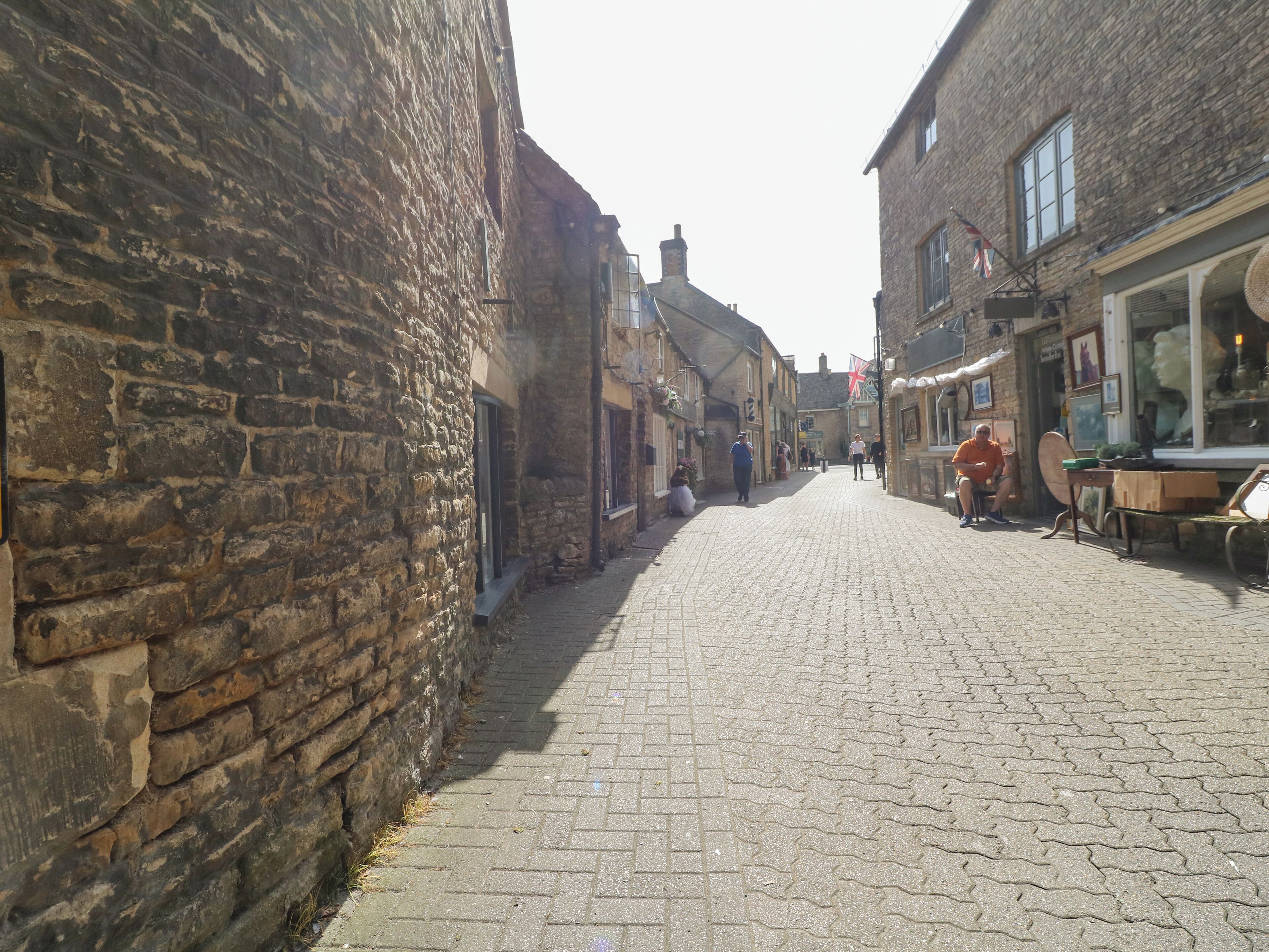 A cobblestone street lined with historic stone buildings, narrow passageways, and a few pedestrians.
