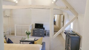 A room with a loft bed, a desk with a computer, a dresser, and a TV. There is a staircase leading to another room. - The Apartment (Cheltenham)