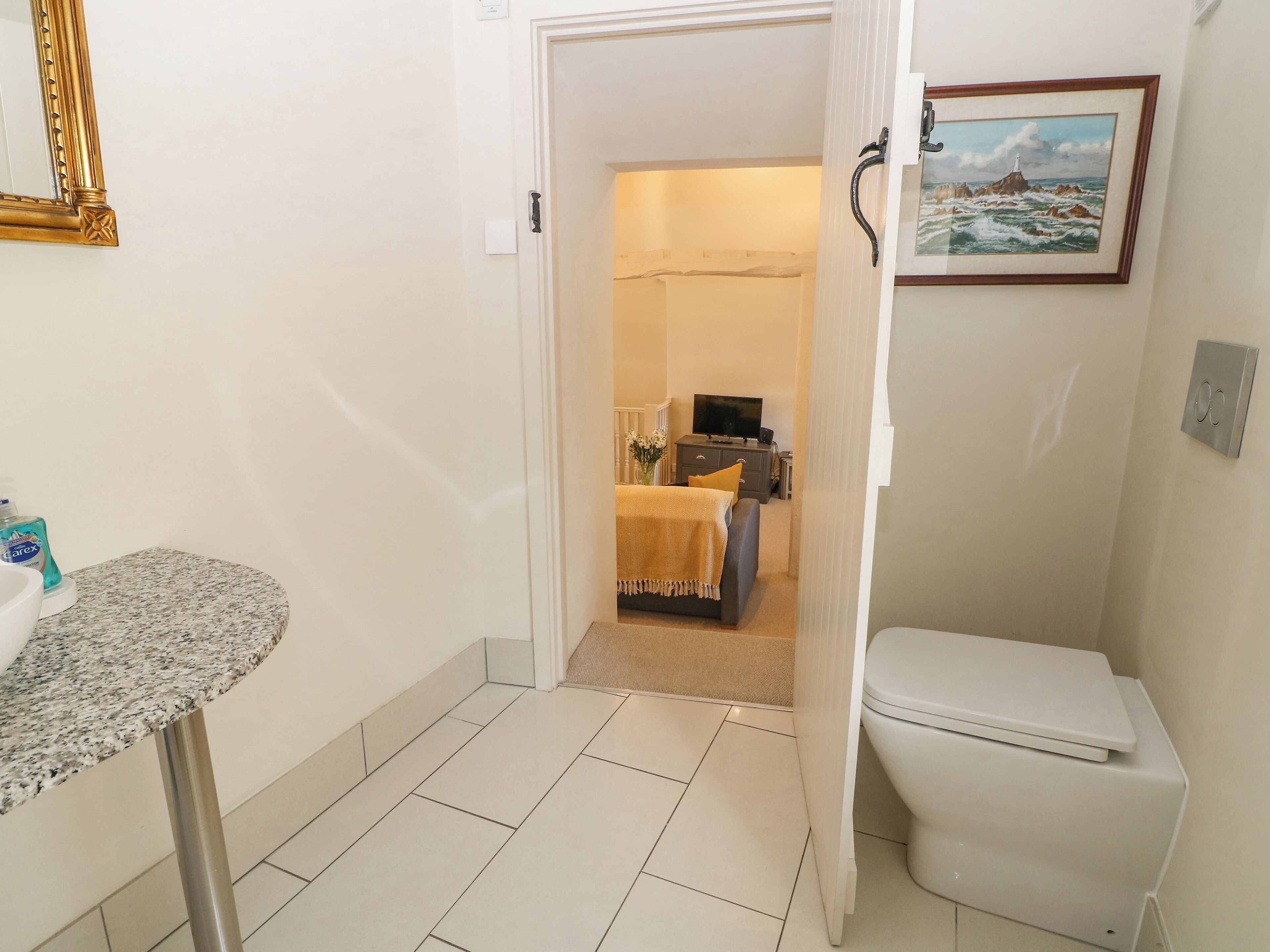 A bathroom with a sink, toilet, and a door leading to a bedroom with a bed and a TV.