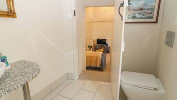 A bathroom with a sink, toilet, and a door leading to a bedroom with a bed and a TV.