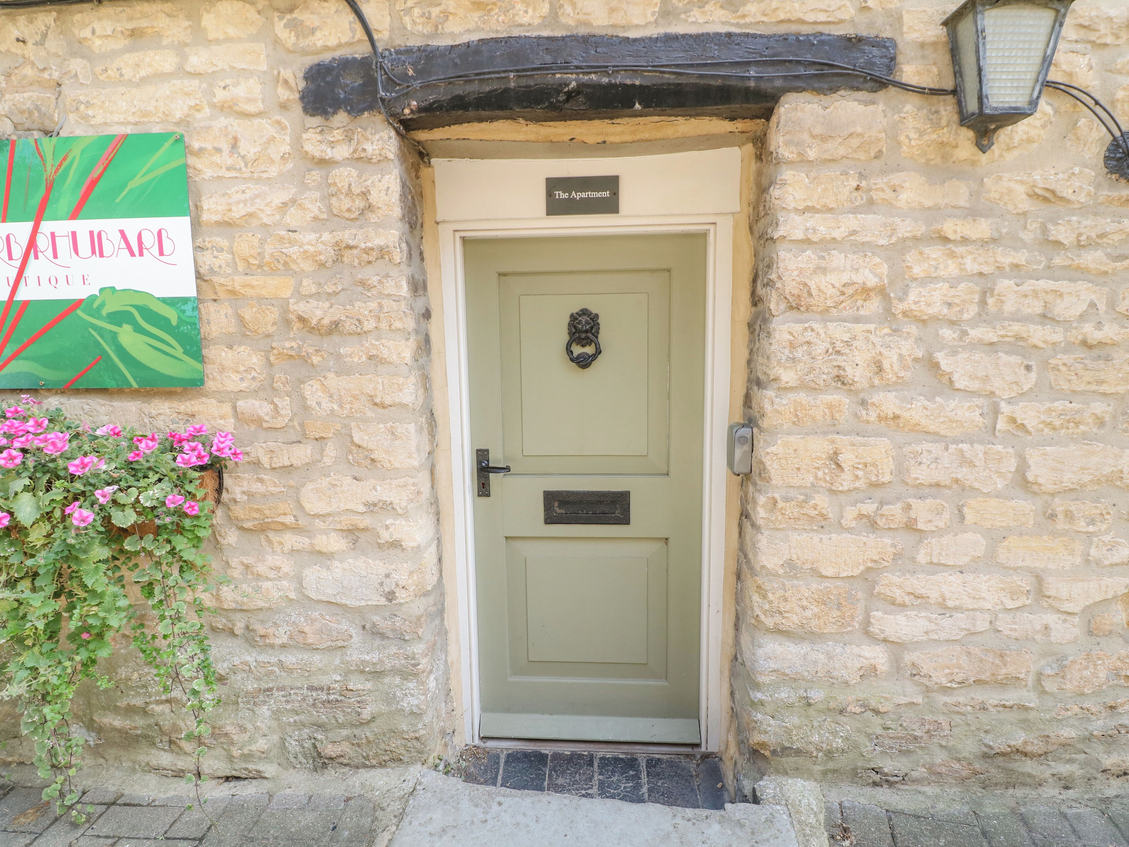 A stone building with a green door, a sign above the door, and a flower box with pink flowers.