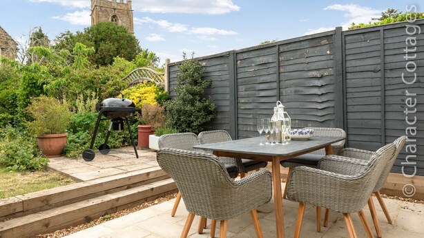 Eine Terrasse im Freien mit Tisch, Stühlen, einem Grill und einem dekorativen Zaun.