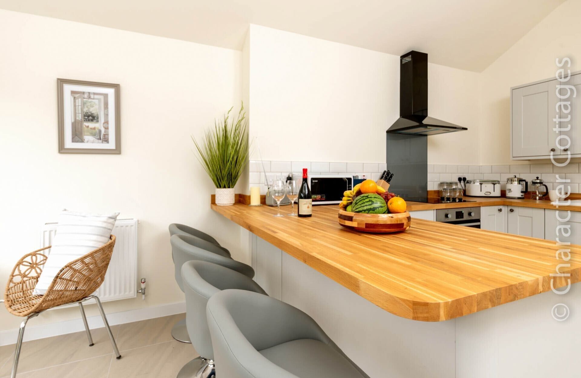 Una cucina moderna con un piano di lavoro in legno, un piano cottura integrato e un forno a microonde. Sul bancone ci sono due sgabelli da bar e una pianta in vaso.