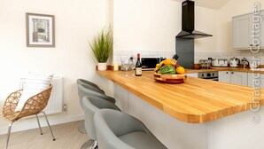 A modern kitchen with a wooden countertop, a built-in stove, and a microwave. There are two bar stools and a potted plant on the counter. - Holly Cottage (Warwick)