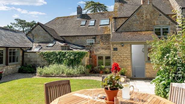 A stone house with a garden patio, a wooden table, and a potted plant. - Copperbeech (Cheltenham)