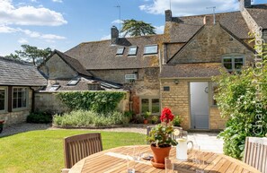 A stone house with a garden patio, a wooden table, and a potted plant. - Copperbeech (Cheltenham)