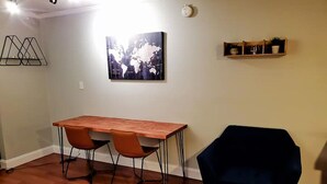 Een kamer met een houten eettafel, twee stoelen, een donkerblauwe fauteuil, een wereldkaart als kunstwerk, een plank met decoratieve objecten en een wandlamp.
