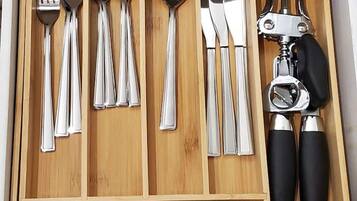 Un cajón con diversos utensilios de cocina, incluyendo tenedores, cucharas, una espátula y un abrelatas.