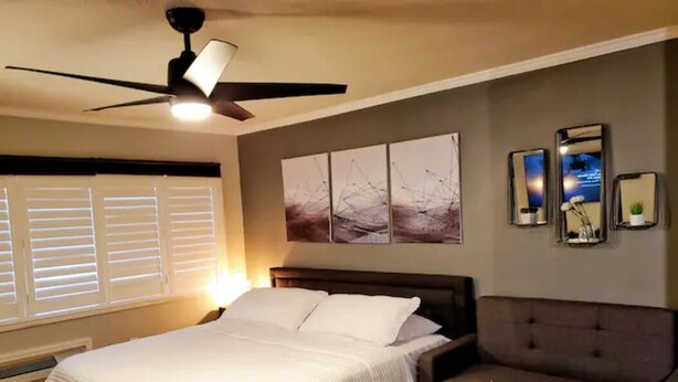 Een slaapkamer met een bed, een plafondventilator, een bank en wanddecoratie.