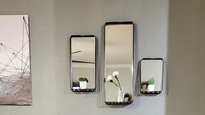 Een kamer met een grijze bank, een ronde tafel met een plant erop, en drie spiegelwanden.