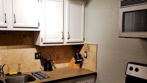 Een keuken met witte kastjes, een zwarte kookplaat en een magnetron.