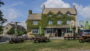 A traditional stone building with ivy-covered walls, outdoor seating, and a pub sign.